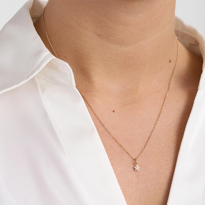 Gouden collier met kleine bloemvormige hanger en diamanten, voorkant op model