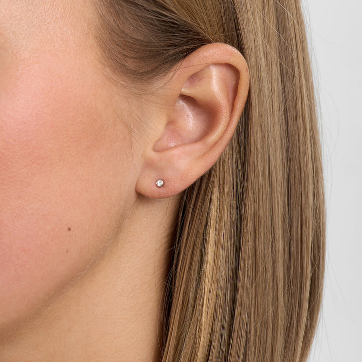 Discrete oorsteker in zilver met heldere steen, vanaf de voorkant op het oor afgebeeld. Eenvoudige en elegante stijl.