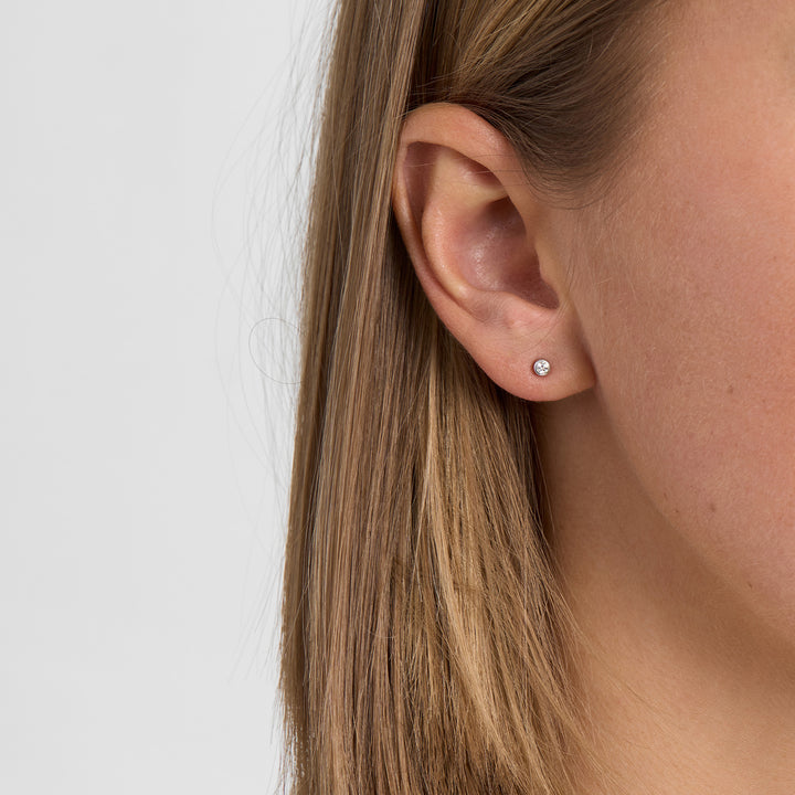 Oorbel van zilverkleurig metaal met enkele heldere steen, vanaf de zijkant op het oor afgebeeld