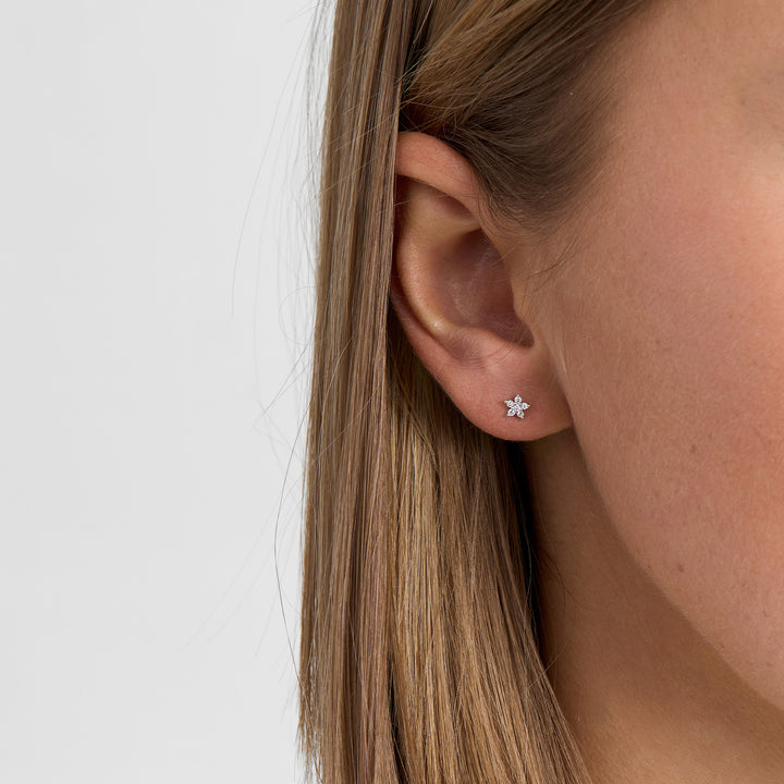 Oorbellen in zilver met bloemvorm en heldere stenen, afgebeeld op het oor, voorkant