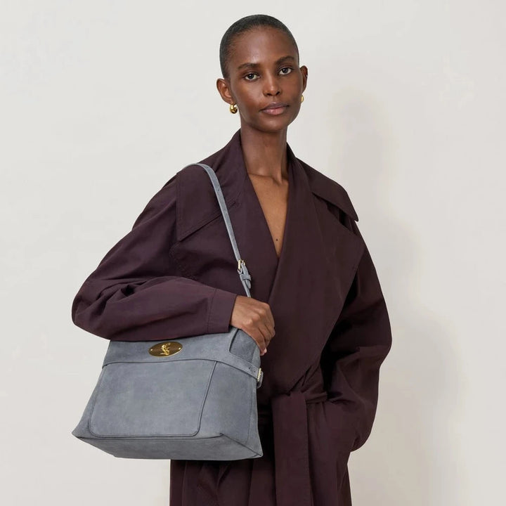 Mulberry taske i grå ruskind med guldfarvet lås, båret af model i mørk lilla frakke. Model 12345