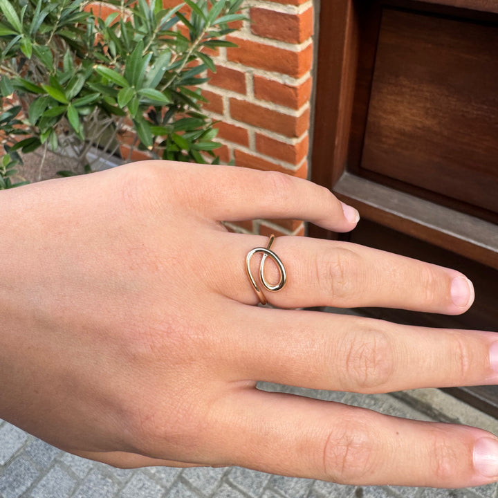 Guldring med et elegant knudedesign, vist på en finger i et naturligt udendørs miljø.