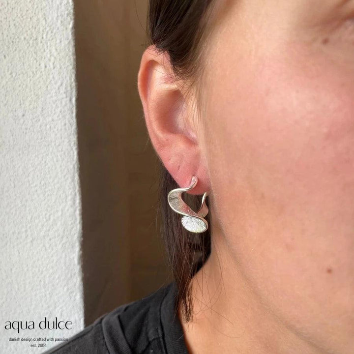 Aqua Dulce Rhumba Medium Hoop in zilver verschijnt op het oor, elegant golvend ontwerp. Model 5319-5319-2
