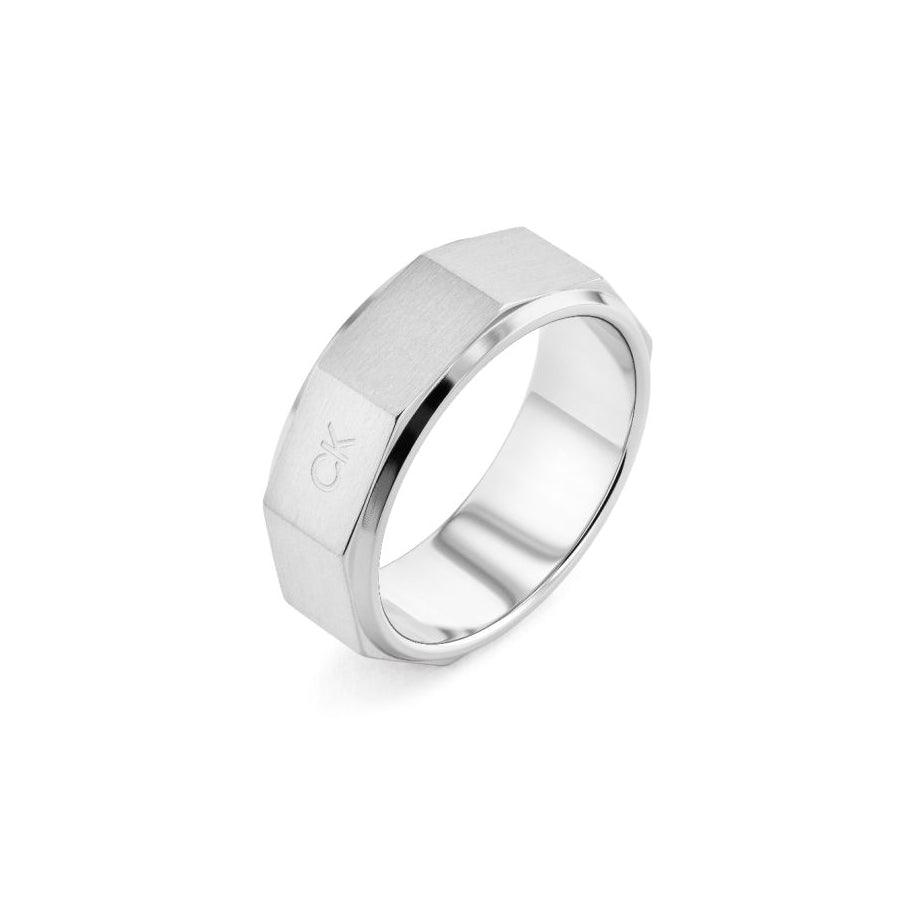 Calvin Klein Latch Ring toont een brede, zilverkleurige herenring van geborsteld staal met een gefacetteerde rand. Model35000316-001.