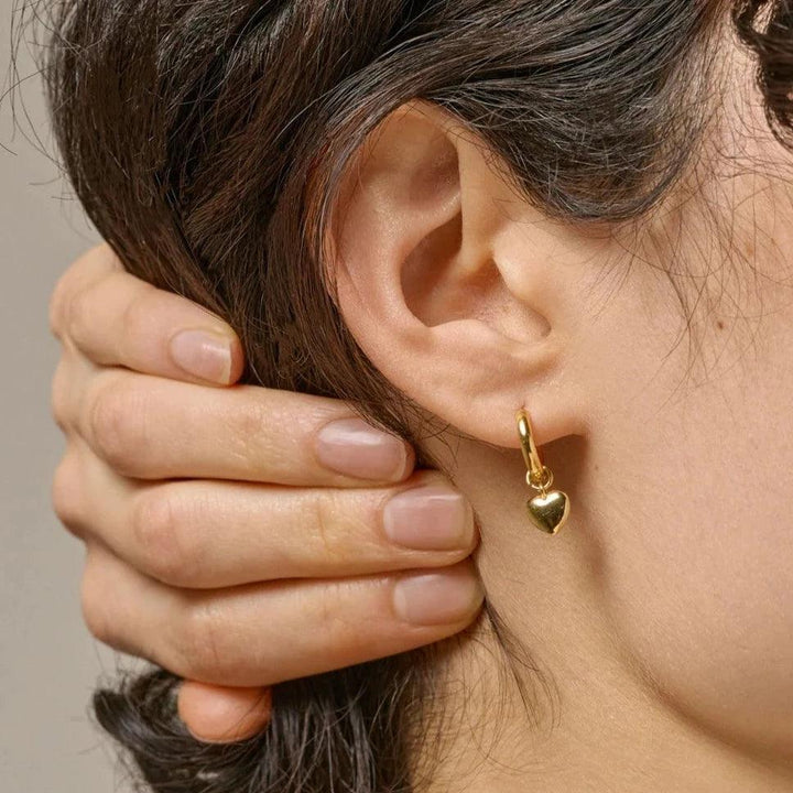 Enamel Amore Gilded Hoops toont een vergulde hartoorbel in het oor van een vrouw. Model e376g-e376g-2