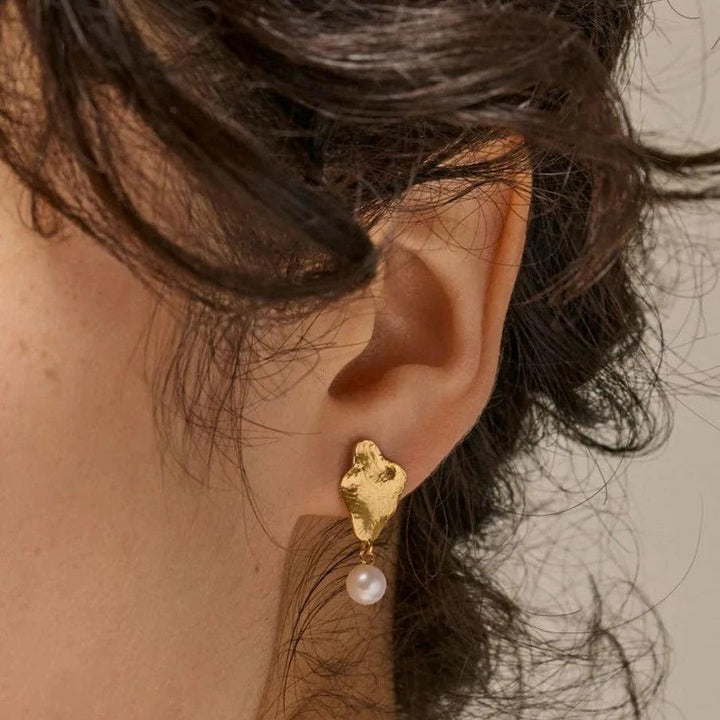 enamel-caia-kleine-oorbellen-e374gm verschijnt op het oor, mat gouden look met hangende witte parel. ModelE374GM