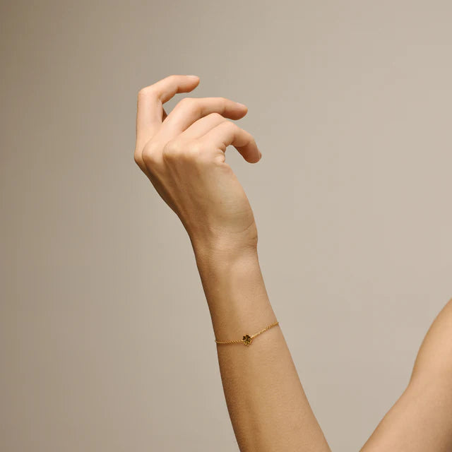 enamel-Klavertje-vier-armband-in-verguld-sol wordt om de pols gedragen, dunne schakelarmband in goudlook met klein klaverdetail. Model b148gm-2