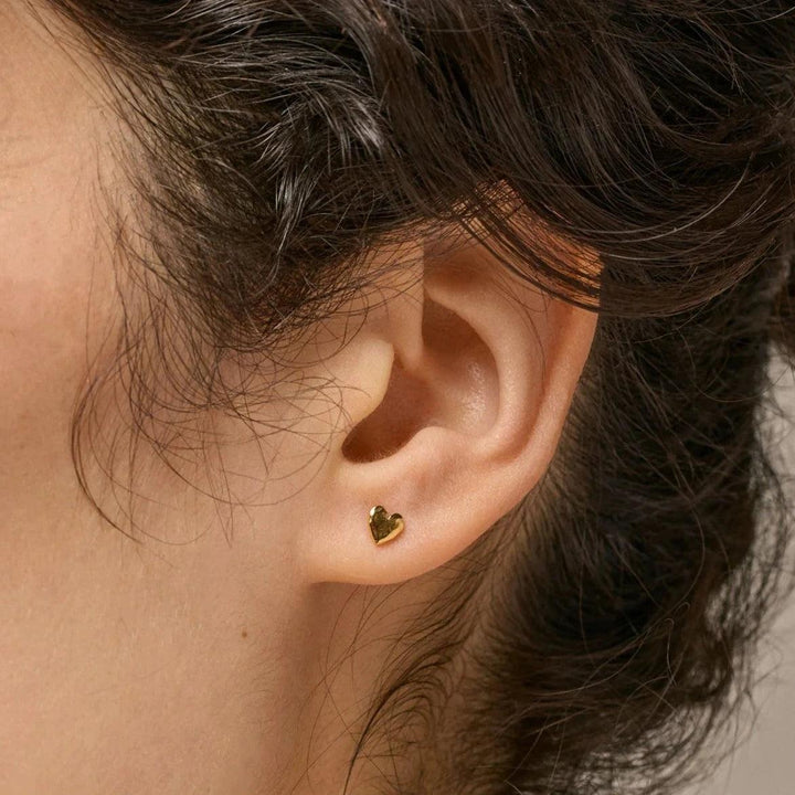 enamel hartvormige studs vergulde hartvormige studs zijn te zien op het oor, klein en glanzend goudkleurig. ModelE373GM