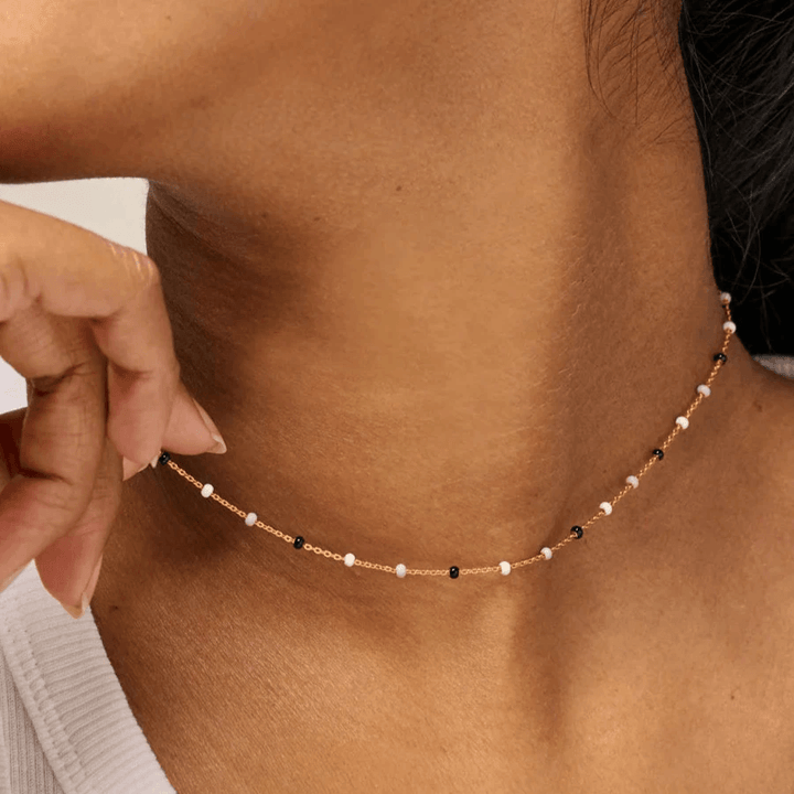 Enamel De Lola Salt n Pepper-ketting wordt rond de nek van het model getoond, een dunne ketting met kleine witte en zwarte parels. Model N55G-ZOUTPEPER