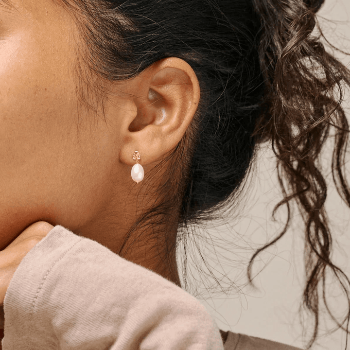 Enamel Poe Pearl Studs worden hier gedragen op het oor, elegante zoetwaterparel en goudkleurige details. Model e384gm-parel