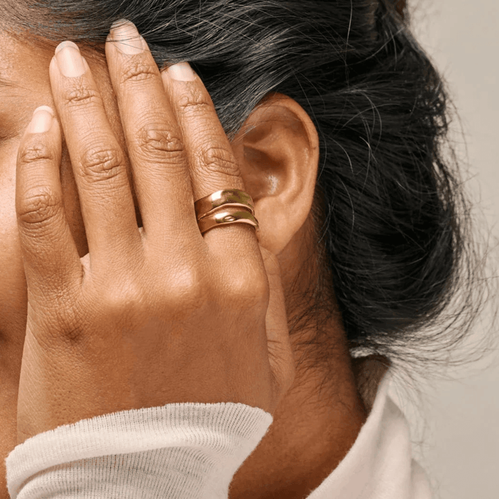 Enamel Sandra Statement Ring verguld verschijnt op de hand van de vrouw dicht bij het oor, glanzend gouden oppervlak. ModelR92G-R92G-001.
