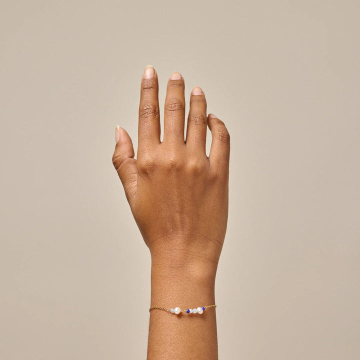 Enamel De Sofia Armband Marine wordt om de pols gedragen, een gouden ketting met witte en blauwe parels. Model b136g-marine