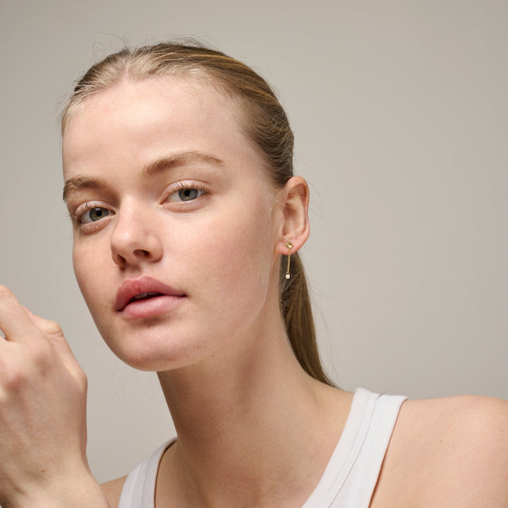 Enamel Sunshine Drop Oorbellen Daisy e423g-madeliefje afgebeeld op model, discrete gouden oorbellen met kleine bloem en druppel. Model e423g-daisy-2.