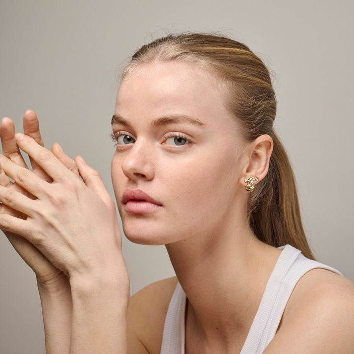 Enamel Sunshine Field Stud e417g wordt gedragen door een vrouw, gouden oorbellen in een organische vorm. Modele417g-2