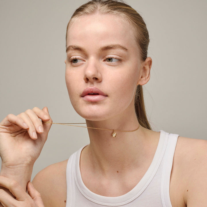 Enamel Sunshine ketting Daisy n136g verschijnt op de hals van het model, gouden ketting met kleine bloemhanger. Model n136g-daisy-2