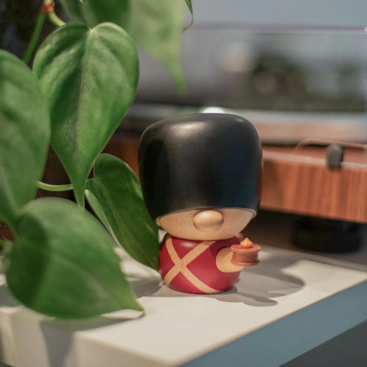 Fablewood HC Andersen's Fyrtøjet-8005-1 houten figuur van bewakers in rood uniform en zwarte berenmuts op plank bij groene plant. Model 8005-1