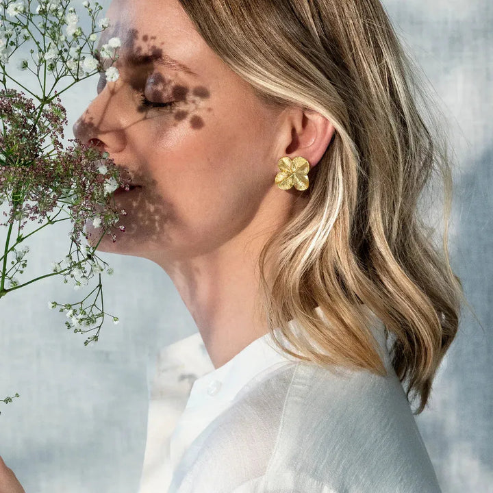 Flora Danica Fir Clover-oorclips gedragen door een vrouw met korte lichte krullen, verguld bloemendetail. Model 907-flc-eaclips-g-2