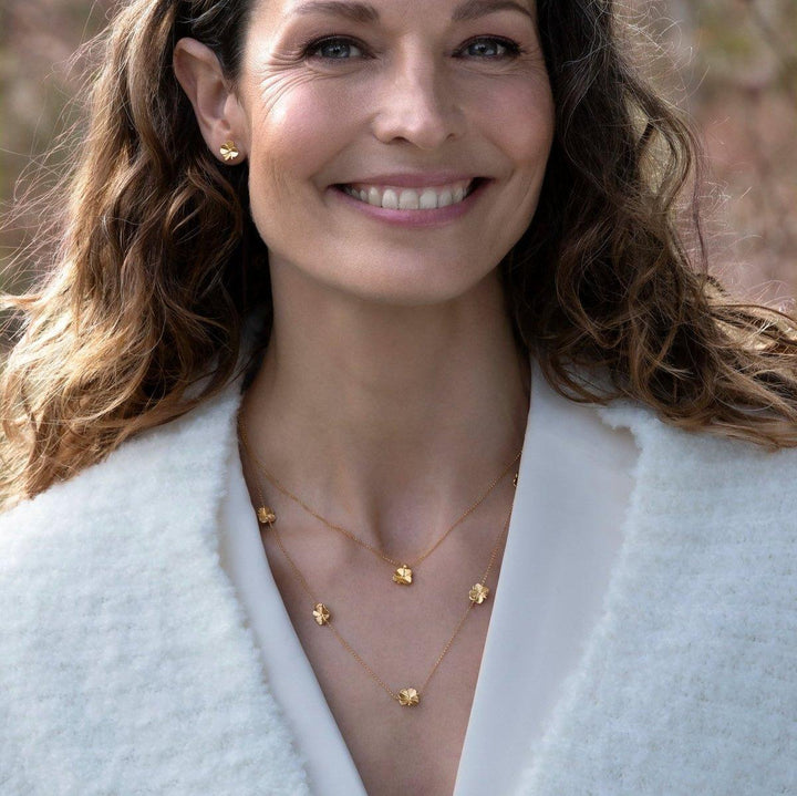 Flora Danica Klavertje vier ketting met vijf klavertjes, gedragen door vrouw, goudlook buitenshuis. Model flc-nelo-g-2