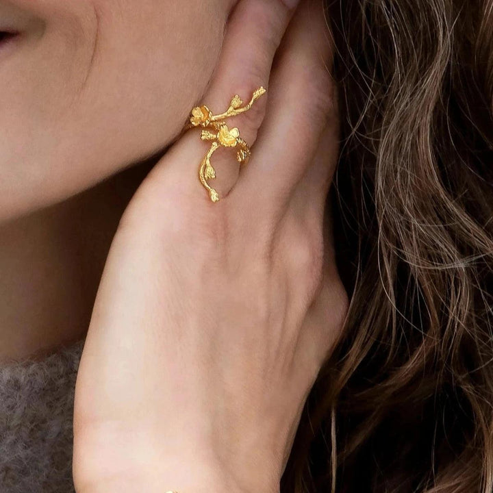 Flora Danica Vergeet-mij-niet-statement-ring weergegeven bij de hand, in glanzende goudkleurige afwerking en bloemmotief. Model FMN-STRI-G-001-2