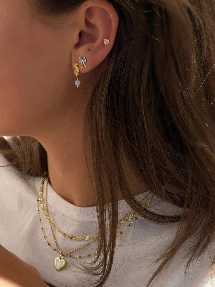 Jeberg Petite Bow blauwe oorknopjes afgebeeld op het oor, blauwe strik in verguld ontwerp, model 52810-2