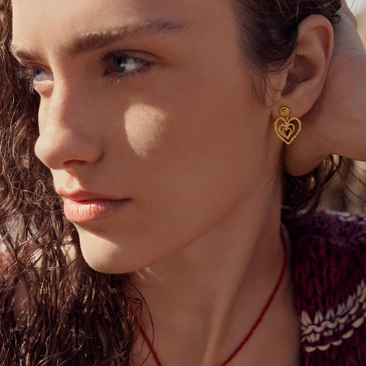 Maanesten Beate Petite vergulde hartoorbellen gedragen door een vrouw, met goudkleurige details, model 10088A