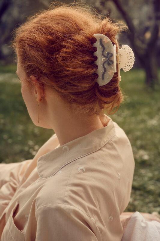 maanesten-desiree-hair-claw-off-white is te zien in het gestylede rode haar van de vrouw, in een zonnige buitenomgeving. Model 3973 - één maat