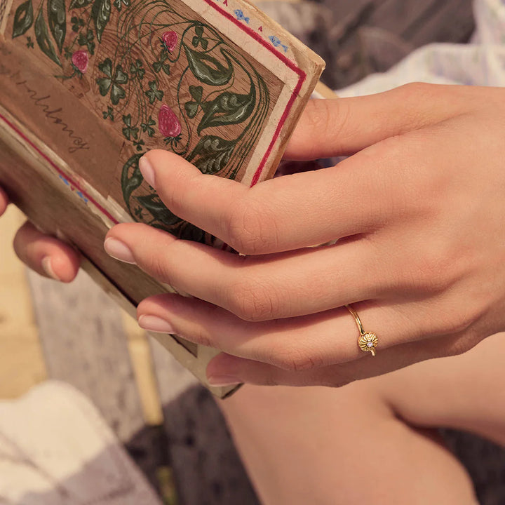 Maanesten Tacita Ring verguld gezien bij de hand in zonlicht, eenvoudige bloemenring in goudlook, Model 4882a-001