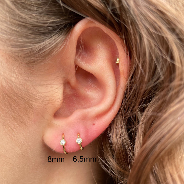 Maria Tash 8 mm Scalloped Diamond Hoop Clicker wordt weergegeven in het oor, goudkleurig en met diamantdetails. Model xrscd-yg-d8-2.