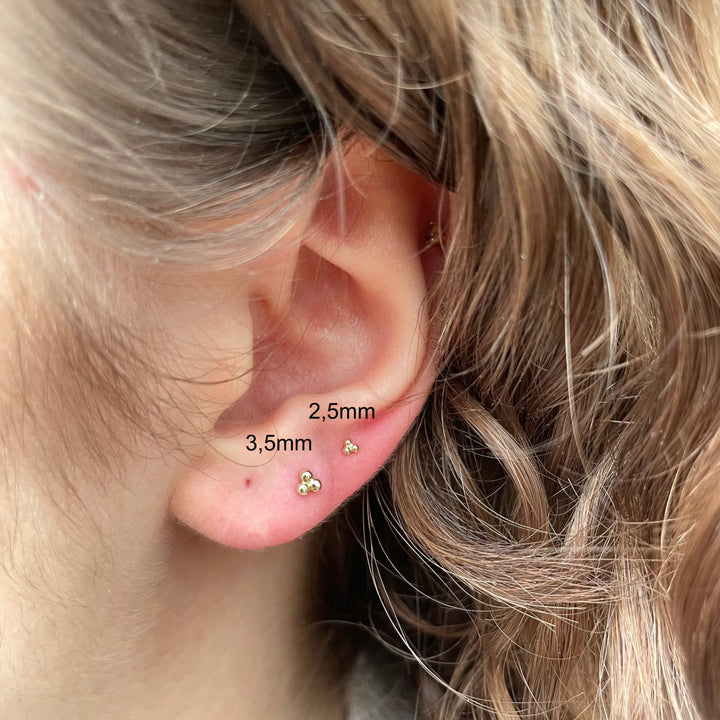 Maria Tash Grote Three Ball Trinity Stud met schroefdraad in goud, gedragen in het oor, minimalistische stijl. Model 35mm-x3btrl-001.