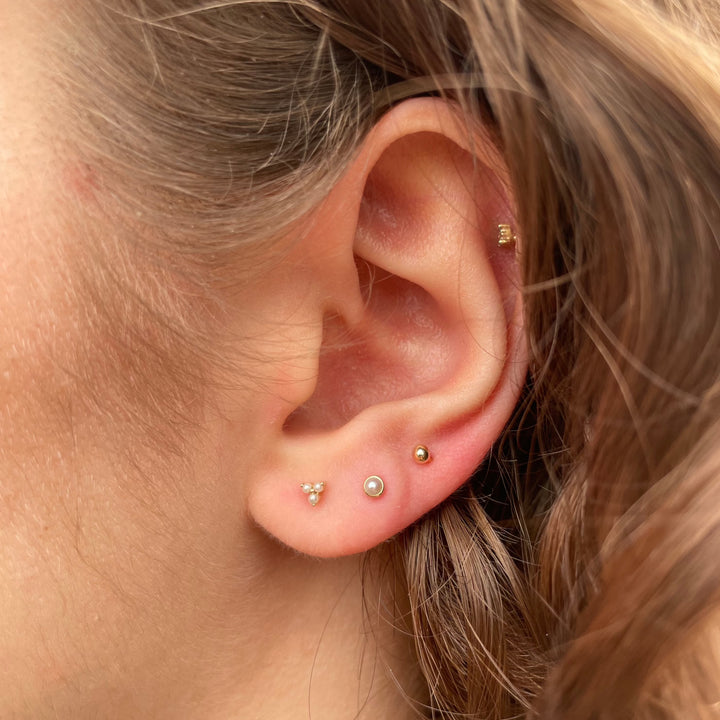 Maria Tash Pearl Trinity Stud wordt in het oor getoond, discreet goud en parels, elegant ontwerp. Model xtrpe-yg-w3-001-2.