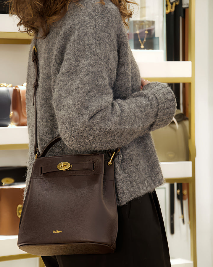 Mulberry Islington Bucket Small Classic Grain Ebony wordt gedragen door een bruine leren damestas met gouden details. ModelHH9390205A110