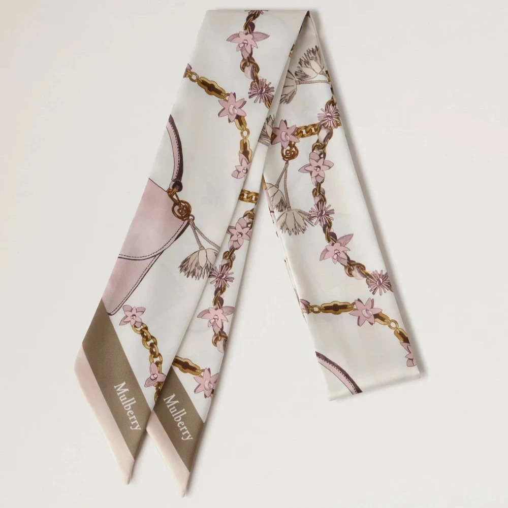 Mulberry Lana Bag and Chains Skinny Scarve Eggshell/Blossom Pink toont een slanke zijden sjaal met roze en gouden kettingdetails. ModelVS4849115W569