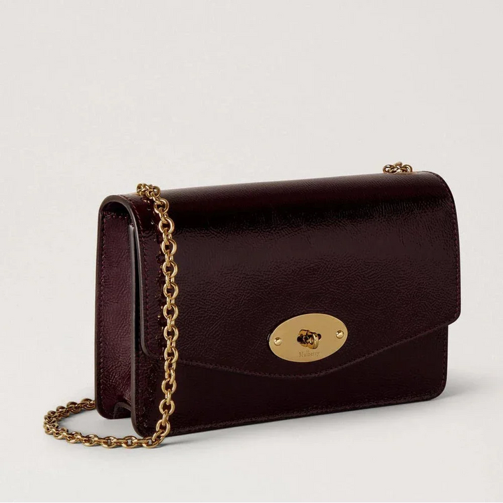 Mulberry Klein Darley Deep Aubergine Patent toont een klein, glanzend schoudertasje in donker aubergineleer met een gouden kettinghengsel. ModelRL8922737V697