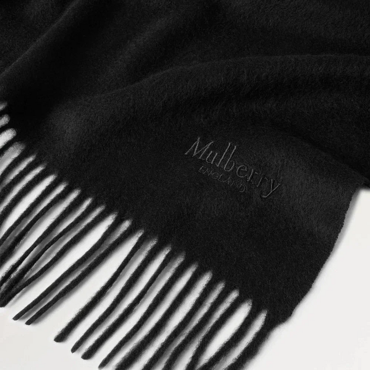 Mulberry Solid Merino Whool Scarf Black toont een zwarte merinowollen sjaal met franjes en discreet logo. Model vs4240947a100