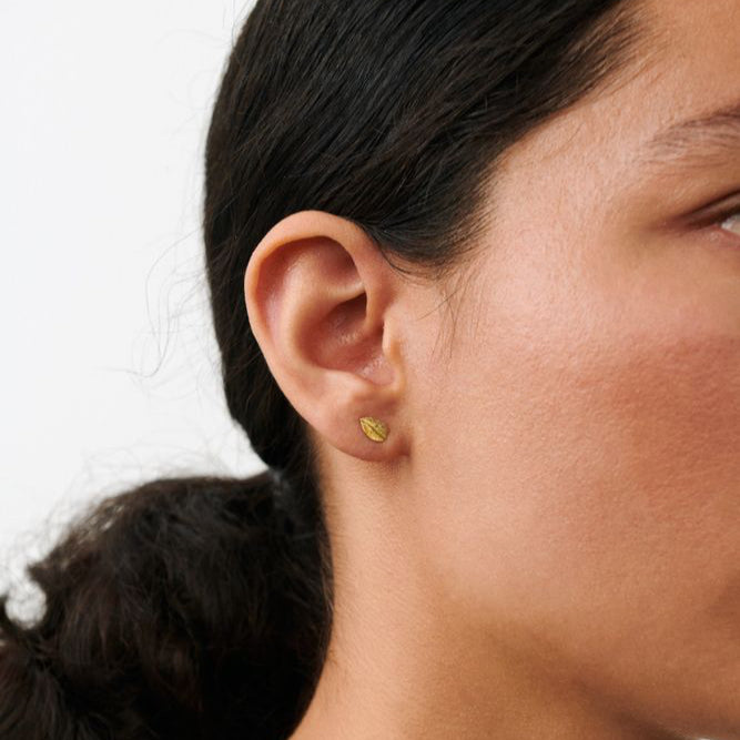 Op het oor zijn Pernille Corydon Elm Leaf-oorstekers in vergulde vorm te zien, discreet bladvormig detail. Model E-329-GP