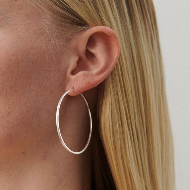 Pernille Corydon Orbit Store Hoops in zilver worden gedragen in het oor van een model met licht haar. Model E-053-S