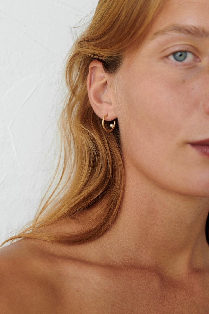Pernille Corydon Pearl Globe Hoops in verguld zilver weergegeven op het oor, elegante en eenvoudige stijl. Model E-404-GP