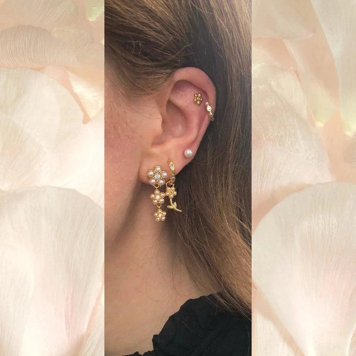 Poppy Stud toont elegante goudkleurige studs met bloemen en pareldetails op het oor, model FW2306-2.