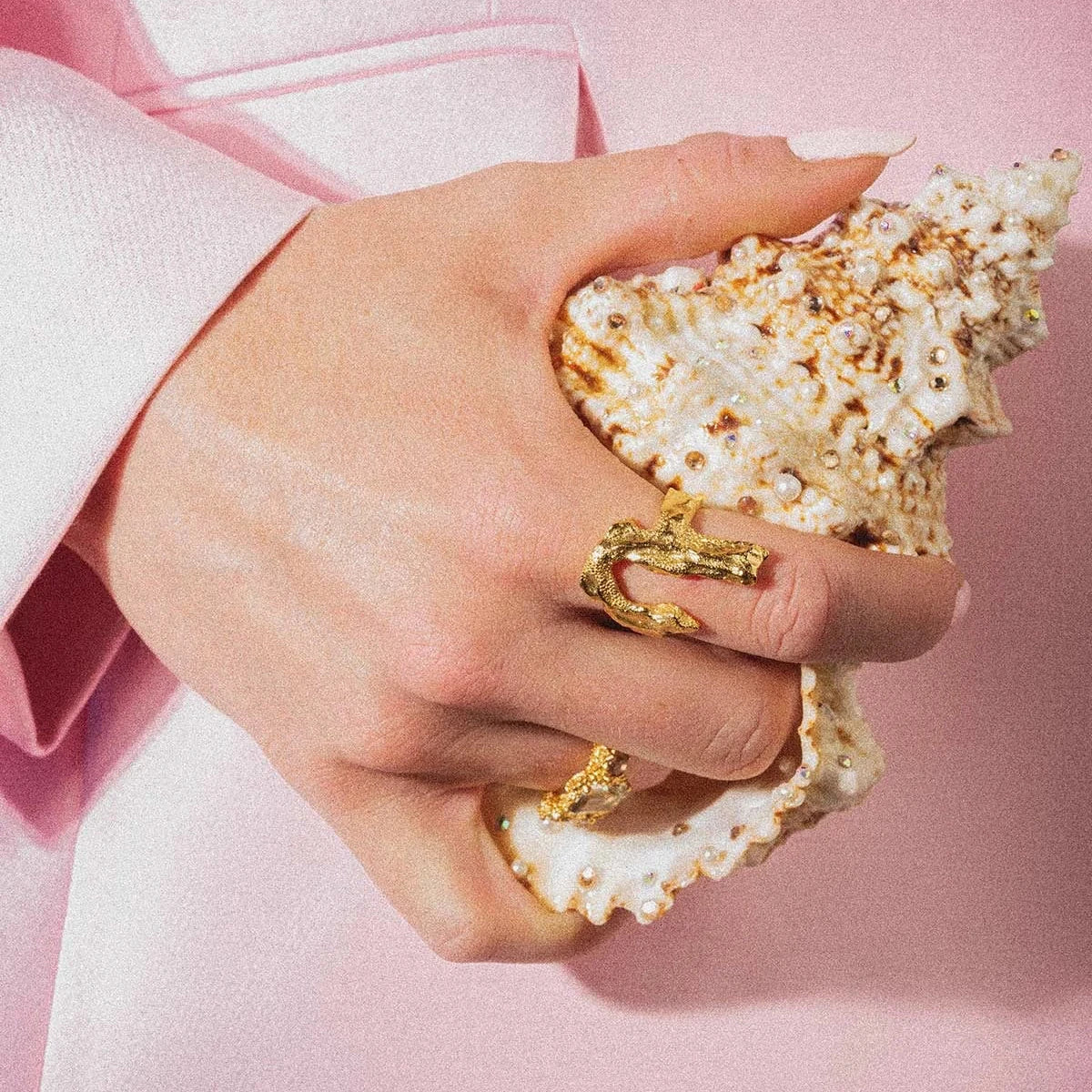 Vincent Bone Vergulde Ring afgebeeld op de hand, detail van goudkleurige ring tegen een schelp. Model vj229-urg-001
