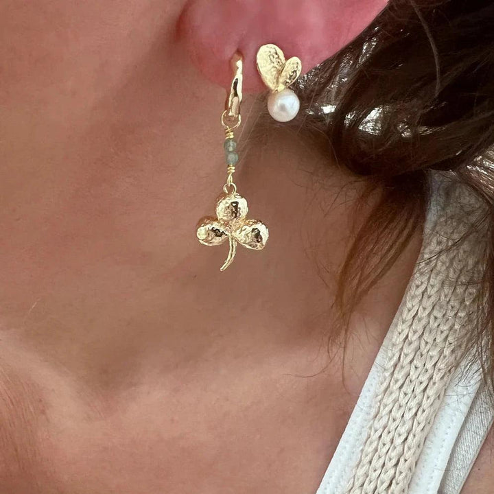 Wioga Madison oorbellen met klaverblad, goudkleurig met pareldetail, zichtbaar op het oor. Model E-8905-gp.