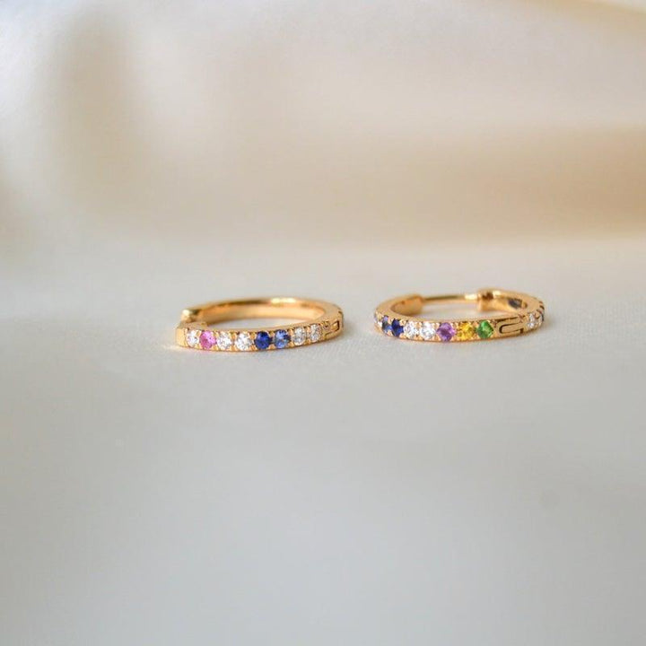 anpe atelier kyra creolen 18kt goud met briljanten en edelstenen, twee oorbellen met gekleurde stenen liggend op een lichte achtergrond. Model 23-2-op maat-1