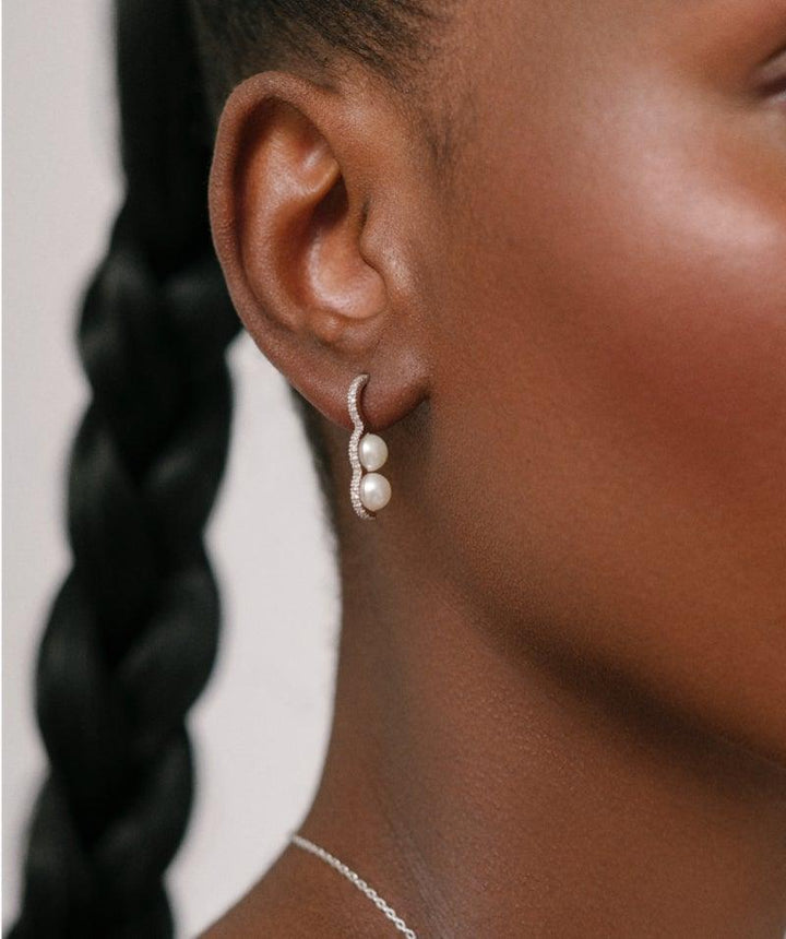 Heriteth Paul x Polar Jewelry Bahati Silver Earring toont een zilveren oorbel met parels die op het oor wordt gedragen, model bah-hs-sl-wp-wz-00502-2.