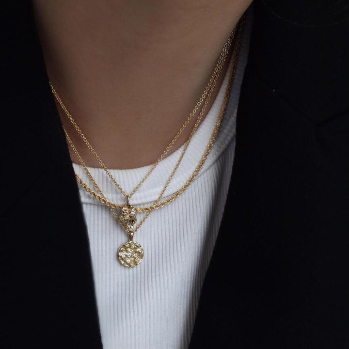 Jeberg Jeberg Jewellery I Am Gold Petite ketting wordt om de nek gedragen met een ronde hanger in goud met een patroon. Model40760-2