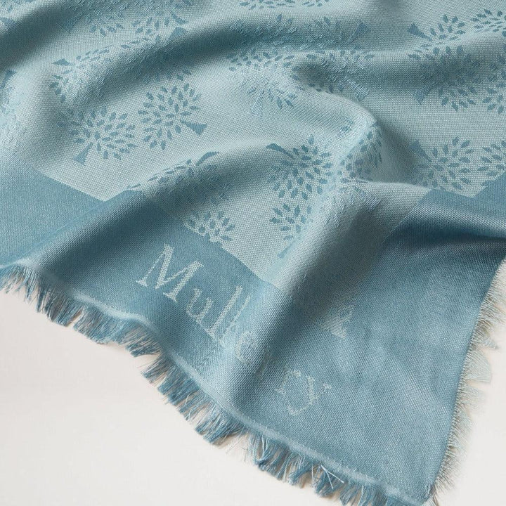 Mulberry Tree Square Silk Organic Cotton Cloud toont een blauwe sjaal met een discreet boompatroon. Model vs4639709d140