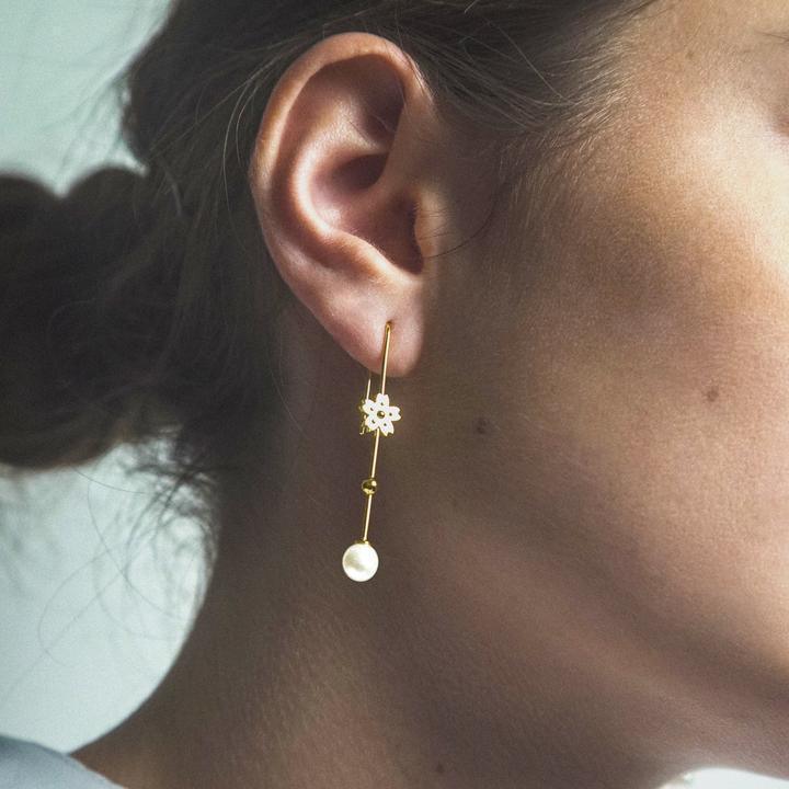 Polar Jewelry Sakura hangende parel vergulde oorbel is te zien op het oor, met gouden bloem en parel. Model SAK-EH-GD-WP-00120
