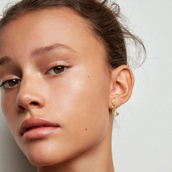 Polar Jewelry The Darning Needle vergulde oorbel op damesoor, elegant gebogen ontwerp. Model dan-st-l-gd-wz-00331-2