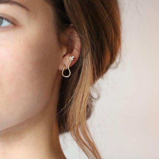 ro copenhagen 18kt Freyd Wave diamanten oorknopje links zichtbaar op het oor, elegant golvend goud en diamanten ontwerp. Model 108104-2